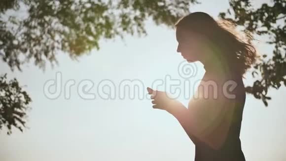 一个年轻女孩的剪影她正在黄昏的阳光下打电话视频的预览图
