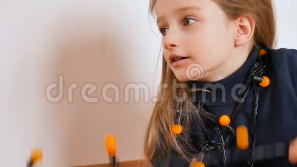 一个金发碧眼的漂亮女孩在玩黄色的圣诞灯和看电视视频的预览图
