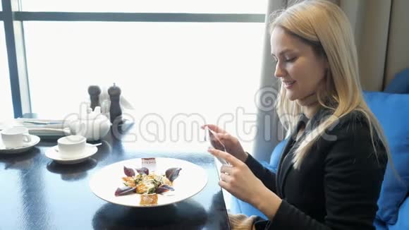 年轻女孩在咖啡厅用现代智能手机拍照食物视频的预览图