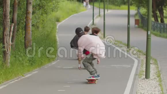 3个年轻人在马路上的绿色公园里玩滑板视频的预览图