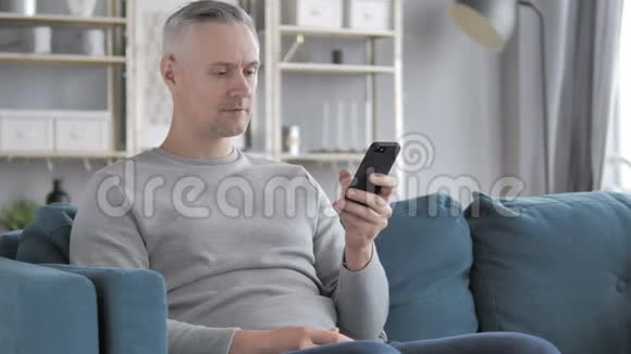 白发男坐在沙发上打电话视频的预览图