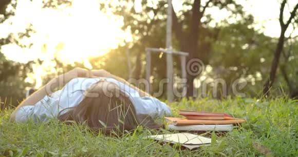 年轻迷人的亚洲女人躺在绿草上日落时用手做心形视频的预览图