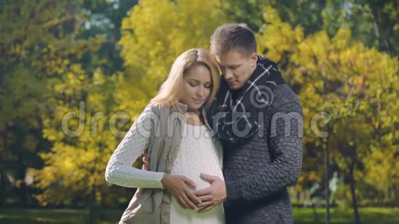 快乐的孕妇和丈夫抚摸着肚子看着相机父母视频的预览图