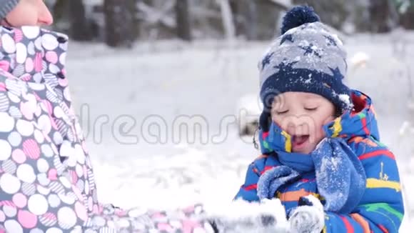 快乐的母子在雪地里玩耍把它扔进照相机里坐在冬天的森林或公园里光线视频的预览图
