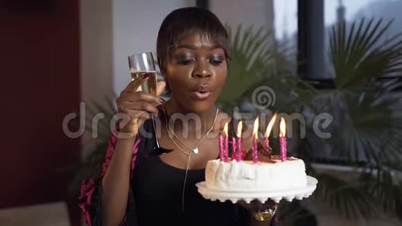 美丽的非洲女孩用香槟杯吹蜡烛在生日蛋糕上视频的预览图