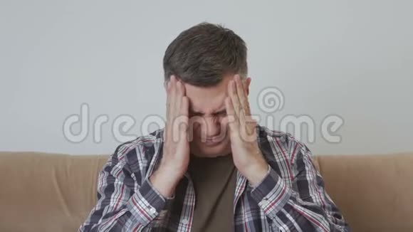一位中年男子坐在沙发上双手捂住头头痛视频的预览图