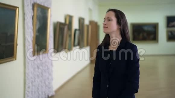 优雅的女孩看着现代艺术博物馆里的照片看艺术作品的年轻女子视频的预览图