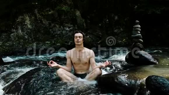 人在一条冰冷的山河里在石头和一个缓慢的洞穴中在莲花的位置上冥想视频的预览图