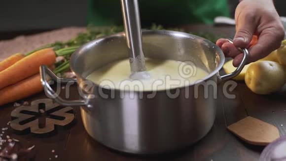 厨师用手搅拌机在金属锅中煮汤煮健康食品捣碎蔬菜全高清道具视频的预览图