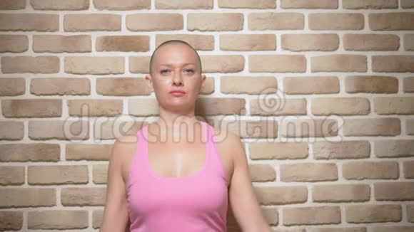 秃顶的女人癌症后的幸存者骄傲地手里拿着一条粉红色的丝带靠在砖墙上视频的预览图