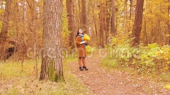 秋天公园里穿着外套和眼镜的年轻女人手里拿着树叶慢动作视频的预览图