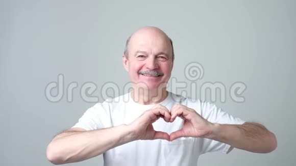 老人用手指微笑着看着相机做着心形的爱标志视频的预览图