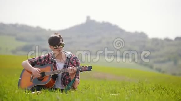 一个年轻人拿着吉他坐在绿色的草地上抽烟视频的预览图