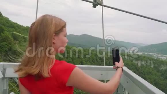 穿着红色T恤的年轻金发女郎在绿色背景下通过智能手机播放视频屏幕断了视频的预览图