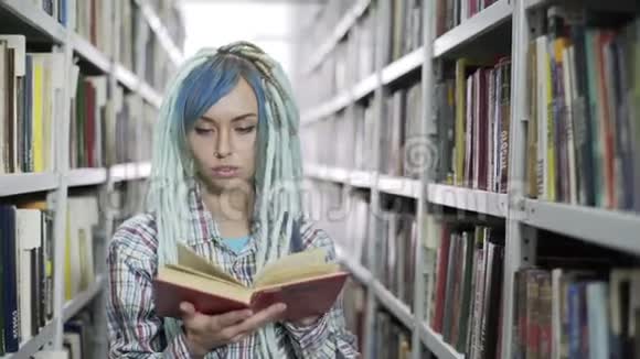 迷人的时髦女学生一边翻阅书一边在有书架背景的图书馆学习视频的预览图