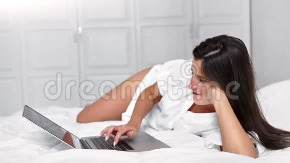 有魅力的欧洲女性周末躺在卧室的床上使用笔记本电脑触摸板视频的预览图