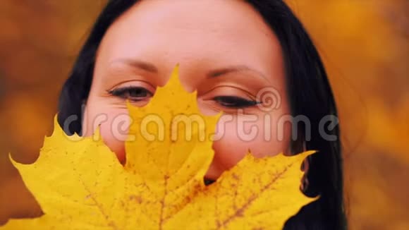 一片枫叶在一个秋天的公园里一个年轻女子的面前视频的预览图