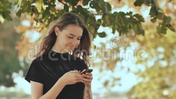 一个年轻的金发俄罗斯女孩在一个夏季公园的电话里写了一条信息视频的预览图