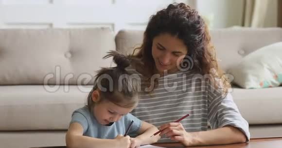 微笑的妈妈在家帮助小女儿用铅笔画画视频的预览图
