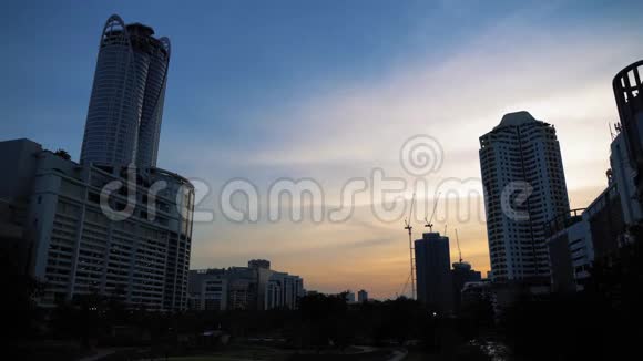 日落时摩天大楼和建筑起重机的剪影城市建筑上美丽的天空背景城市视频的预览图