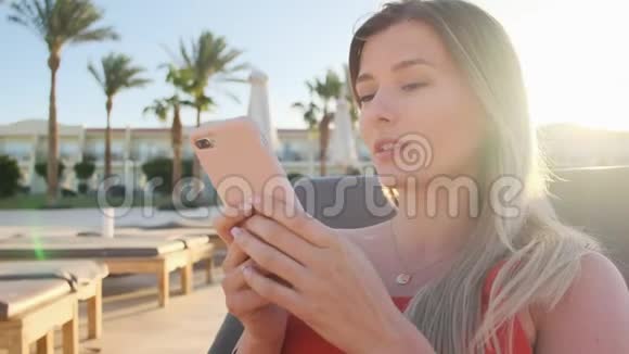 女性使用智能手机在躺椅上休息的肖像浏览互联网通过社交媒体滚动青年视频的预览图