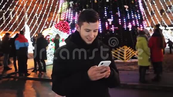 时尚男士在圣诞夜使用手机手机应用程序街道上装饰着新年晚会视频的预览图
