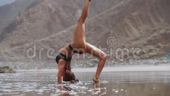 在海边做瑜伽的女孩站在平衡器里站在他的手上休息视频的预览图