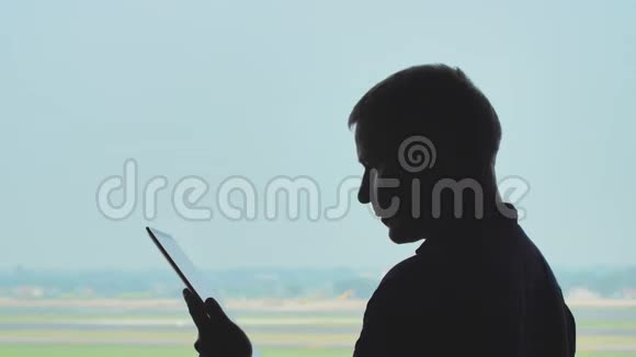 年轻人在飞机起飞的背景下使用平板电脑的剪影视频的预览图