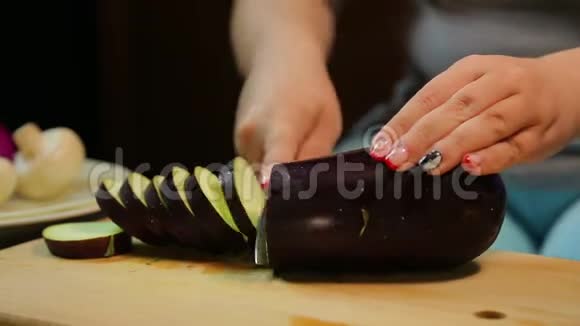 女人的手正在用一把刀在木板上切割一个深色的茄子视频的预览图