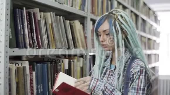 迷人的时髦女学生一边翻阅书一边在有书架背景的图书馆学习视频的预览图