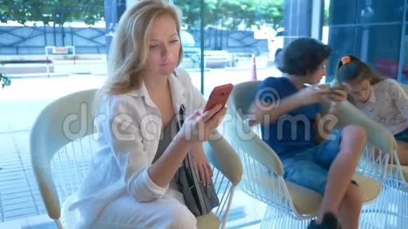 一位忙碌的女士在酒店大堂使用电话她的孩子坐在她旁边也使用电话视频的预览图