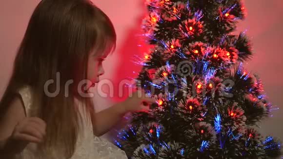 女儿在圣诞树上检查花环小孩子在儿童房的圣诞树旁玩耍美丽的人造的视频的预览图