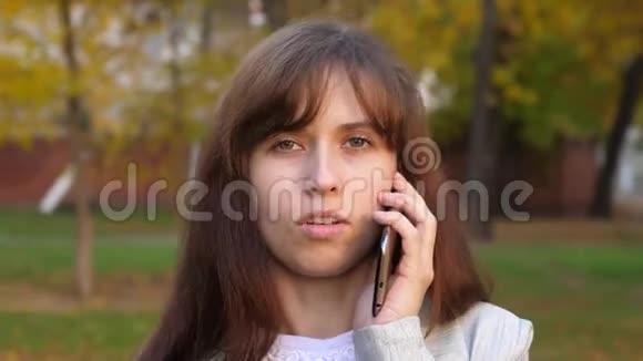 年轻的女孩在电话里交谈在城市公园里笑容满面视频的预览图