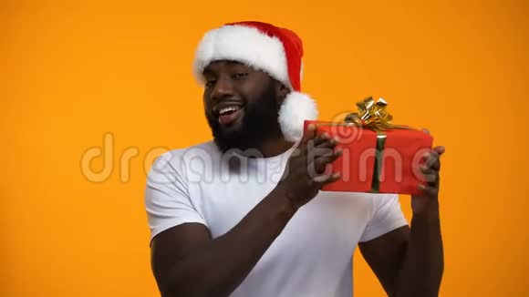 戴圣诞帽的美国黑人男子手里拿着圣诞礼物眨眼度假视频的预览图