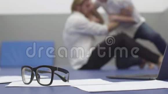 背景中两个穿着白色衬衫的男人在地板上摔跤的模糊身影文件笔记本电脑和眼镜视频的预览图