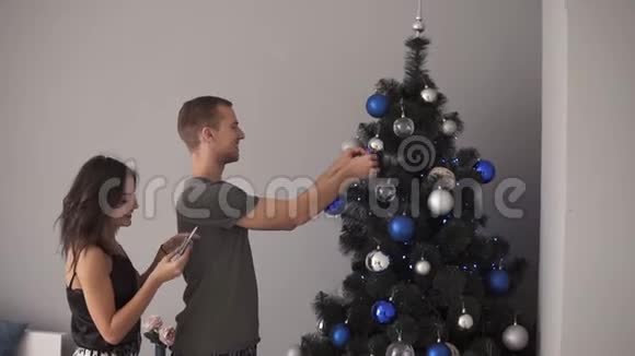 年轻夫妇为新年或圣诞节做准备拥抱站在杉树旁边装饰它视频的预览图