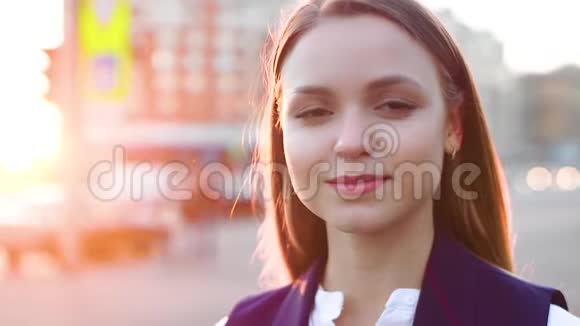 美丽的年轻女孩看着相机微笑着理顺头发晚上在市中心视频的预览图