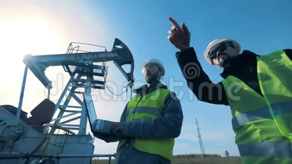 带着笔记本电脑的人走在石油井架附近化石燃料石油工业理念视频的预览图