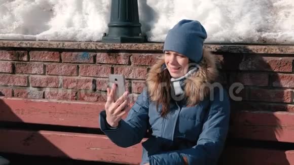 一个女人坐在冬季公园里用手机聊天视频的预览图