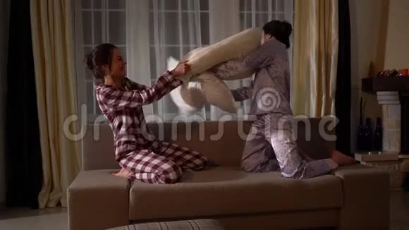 晚上姐妹双胞胎在舒适的客厅里笑着和枕头打架视频的预览图