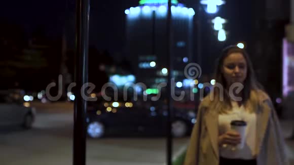 迷人的女孩带着咖啡晚上沿着马路穿过城市视频的预览图
