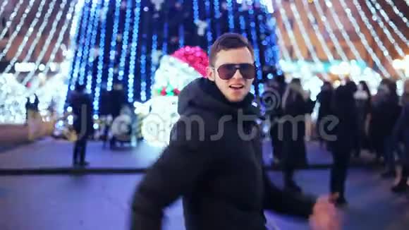 戴着眼镜的时髦男人在城市圣诞树的新年派对上滑稽地跳舞视频的预览图
