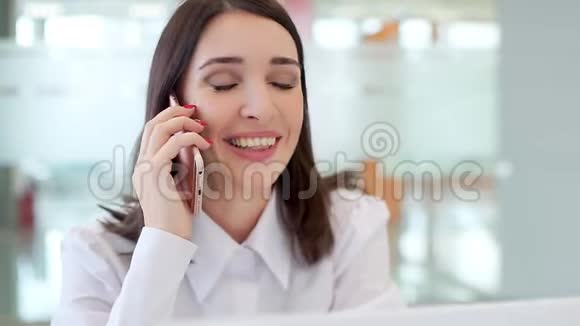 一个女孩在一个明亮的办公室工作在笔记本电脑和电话交谈微笑视频的预览图