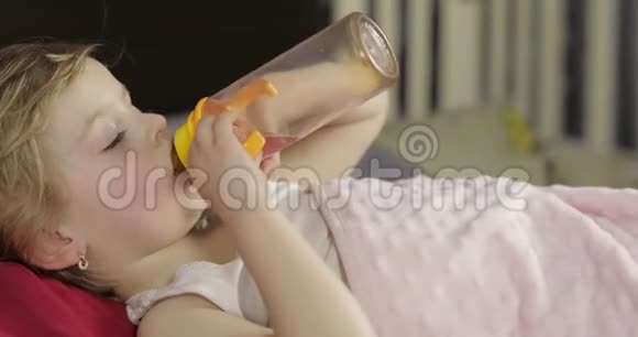 可爱的女婴睡在家里舒适的床上喝着瓶子里的果汁视频的预览图