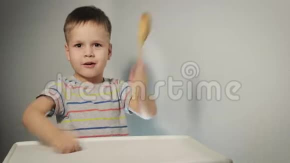 一个小而有趣的男孩敲着桌子上的勺子要求吃饭视频的预览图