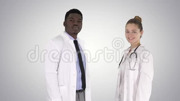 两个白种人和非裔美国人微笑的医生站在镜头渐变背景视频的预览图