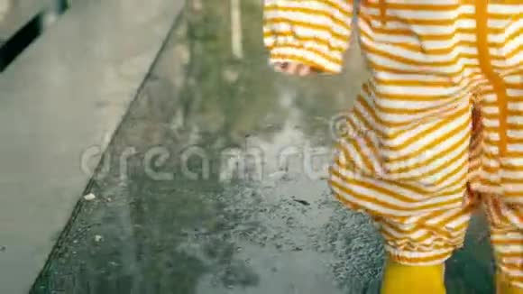 小宝宝穿着橙色条纹防水雨衣和黄色橡胶雨靴在雨后的水坑上散步特写镜头视频的预览图