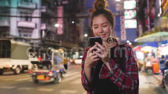 年轻的亚洲女性在城市的夜晚使用智能手机模糊的夜晚繁忙的路灯背景视频的预览图