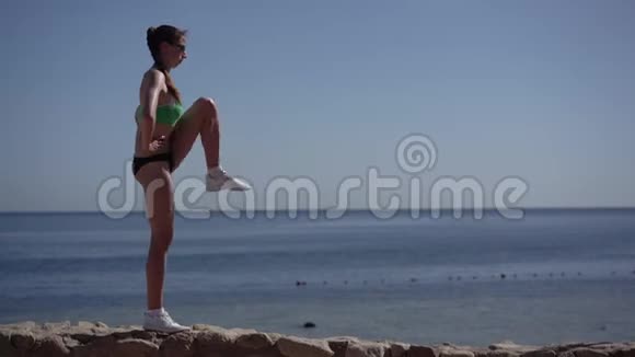 瘦女人慢跑者在海滩上热身她的腿视频的预览图