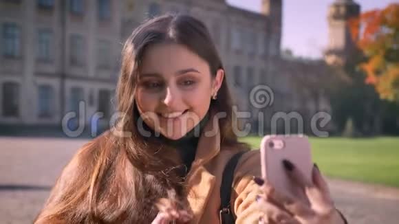 可爱微笑的白种人女孩带着快乐的微笑一边站着一边拿着手机视频的预览图